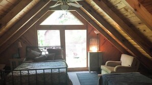 A cozy attic bedroom with a bed, a chair, and a heater. - Quaint Cabin in the Trees!
 (Counce)
