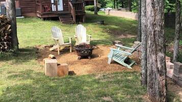 A wooden cabin with a porch, two Adirondack chairs, a fire pit, and a small table.