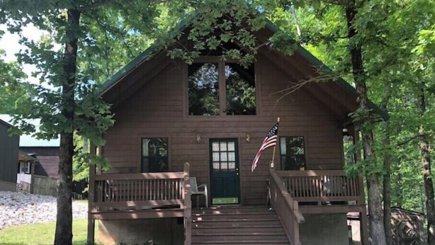 A rustic cabin with a front porch, a front door, and an American flag. - Quaint Cabin in the Trees!
 (Counce)