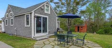 A house with a stone patio, a barbecue grill, and a small shed.