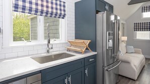 Eine Küche mit einem Edelstahl-Kühlschrank, einem Spülbecken mit Holzablage und einem Fenster mit kariertem Fensterladen.