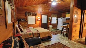 Una habitación acogedora tipo cabaña, con una cama, kitchenette pequeña y zona de comedor.