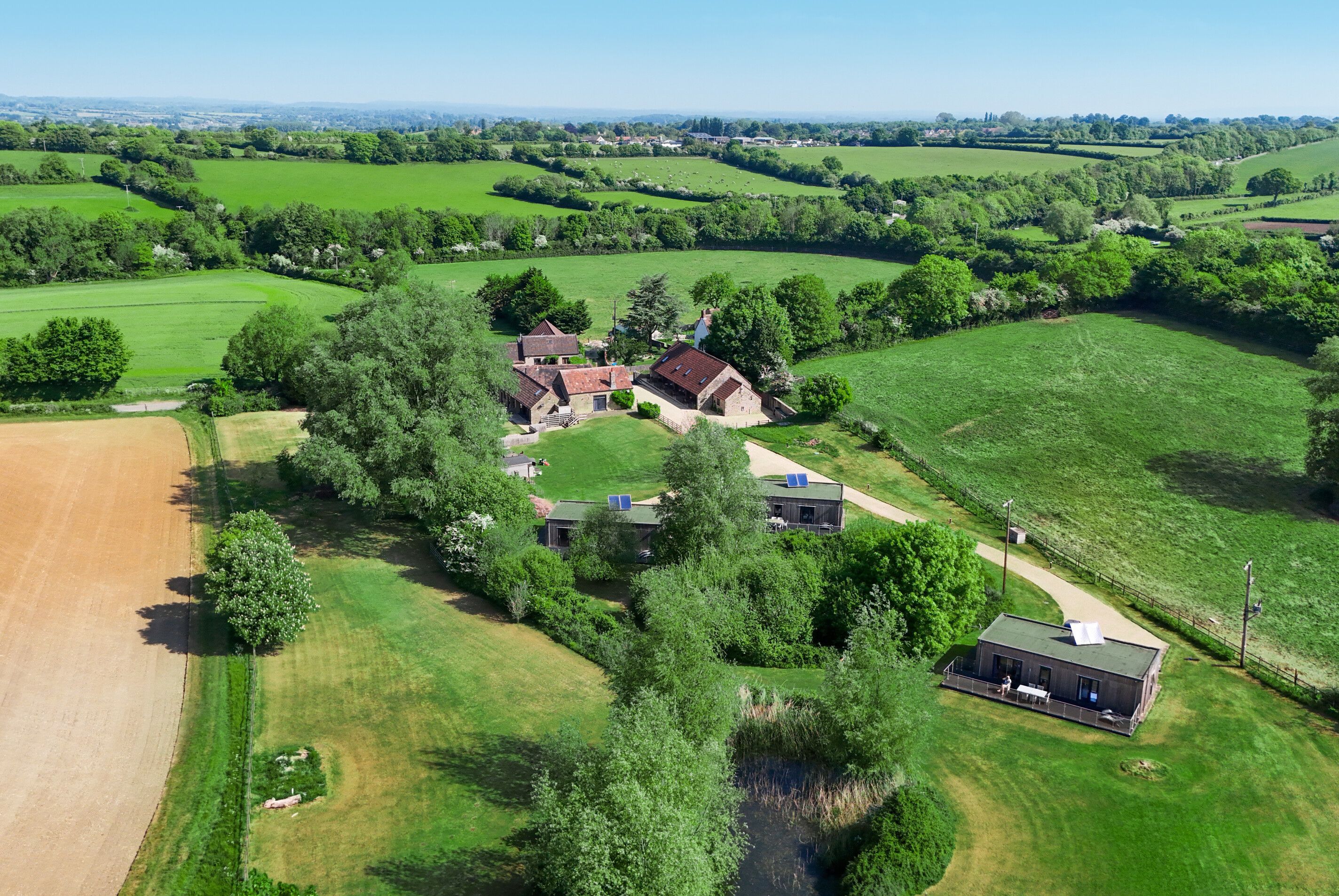Luchtbeeld van een landelijk gelegen pand met meerdere gebouwen, waaronder een hoofdgebouw met een ruime tuin en aangrenzende kleinere constructies.