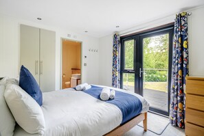 A bedroom with a bed, a wooden wardrobe, a bathroom with a toilet and sink, and a balcony with curtains. - Farleigh Lodge - A peaceful,  rural retreat on the outskirts of Frome, near Longleat Safari Park and (Beckington)