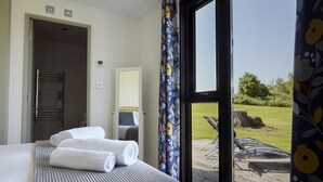 A hotel room with a bed, a bathroom, and a view of a lawn and chairs outside. - Nunney Lodge - A peaceful, rural retreat on the outskirts of Frome, near Longleat Safari Park and Ba (Beckington)