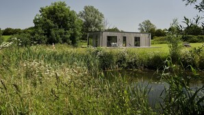 A modern, minimalist house with a flat roof, large windows, and a patio area with outdoor furniture. - Nunney Lodge - A peaceful, rural retreat on the outskirts of Frome, near Longleat Safari Park and Ba (Beckington)