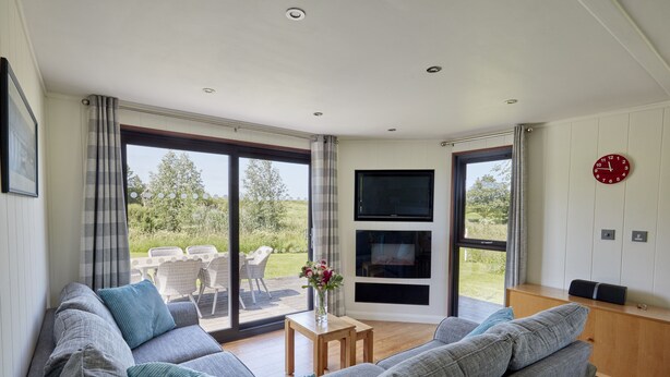 A modern living room with a grey sofa, a wooden coffee table, and a TV mounted on the wall. - Nunney Lodge - A peaceful, rural retreat on the outskirts of Frome, near Longleat Safari Park and Ba (Beckington)