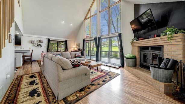 A spacious living area with a large window, a fireplace, and a television mounted on the wall.