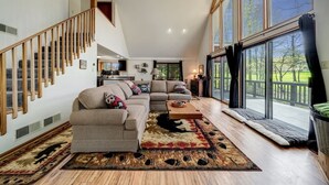 A spacious living room with a large sofa, a coffee table, and a view of the outdoors through large windows.