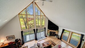 A spacious loft-style living room with large windows, a fireplace, and a ceiling fan.