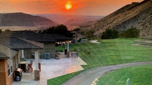 A residential property with a driveway leading to a covered patio area, a lawn, and a hilly landscape in the background. - C03 Spacious 3BR Townhouse on the Golf Course (Quincy)