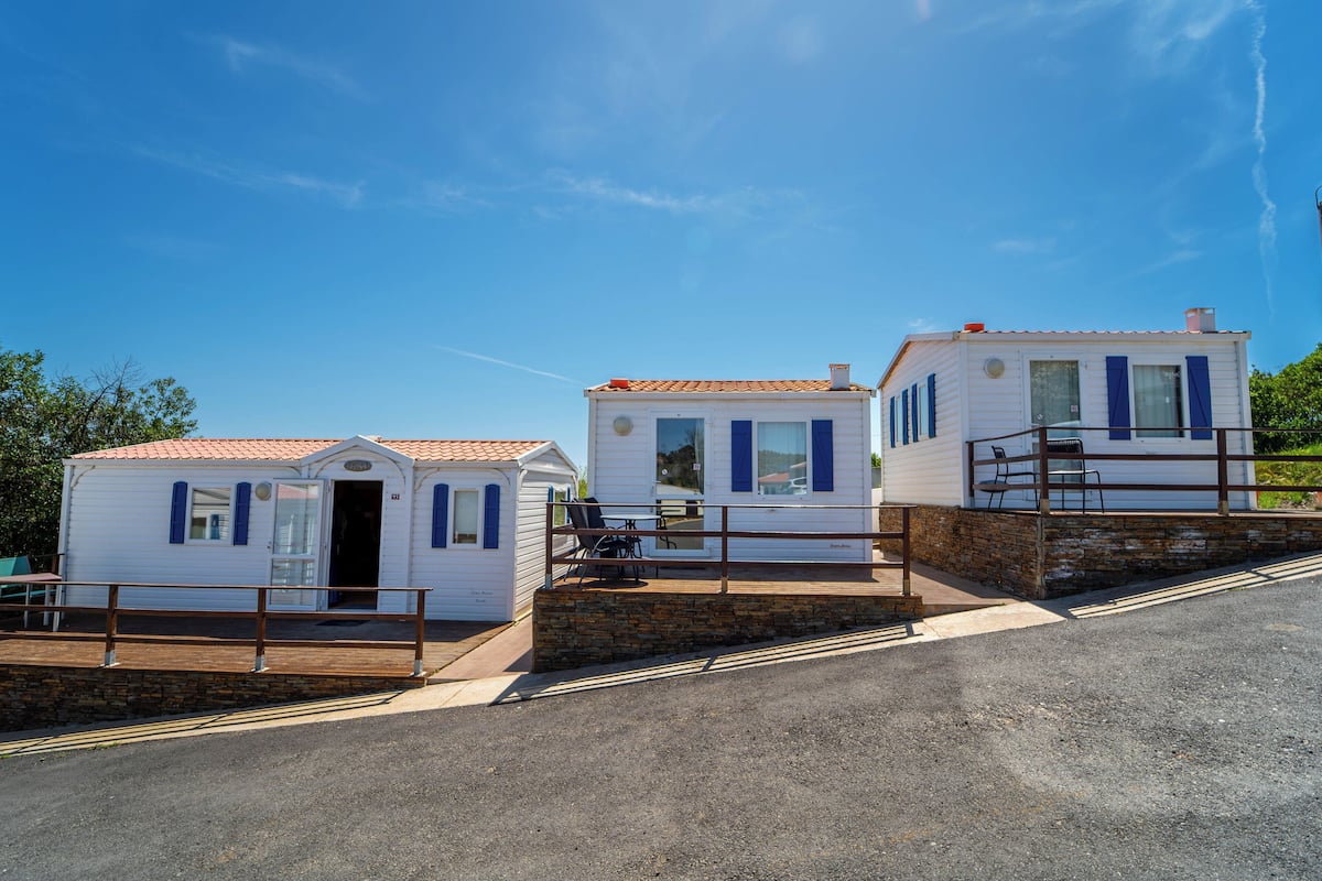 Three white mobile homes with blue shutters, each with a small porch and a chair.