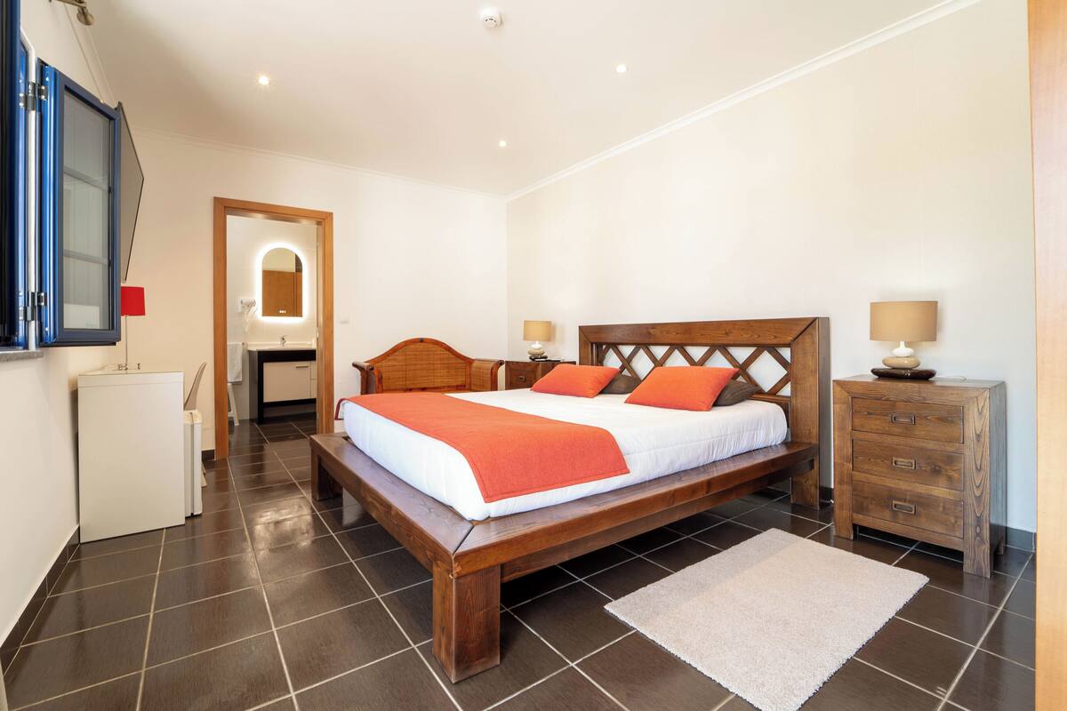 A bedroom with a wooden bed, a bedside table, a nightstand, and a mirror.