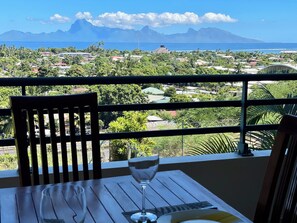 Un balcon avec une table et une chaise en bois, donnant sur une ville côtière avec des montagnes en arrière-plan.