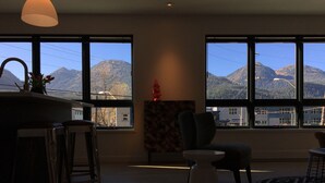 A modern interior with large windows offering mountain views, a kitchen area, and a seating space with a small table. - Chalet Suite in Downtown Juneau (Juneau)