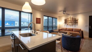 A modern kitchen with a large island, stainless steel appliances, and a view of the city through large windows. - Chalet Suite in Downtown Juneau (Juneau)