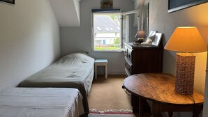 A small, cozy bedroom with two single beds, a wooden dresser, a lamp, and a window offering a view of the outside. - House for rent for eight people with garden and beach access (ARZON)