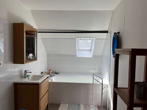 A small, modern bathroom with a white sink, vanity, and bathtub. There is a skylight window and a small shelf with a bucket. - House for rent for eight people with garden and beach access (ARZON)
