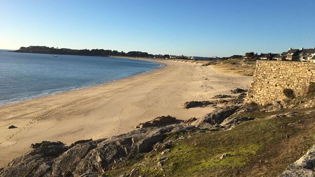 A coastal beach with a stone wall and buildings in the background. - Maison Proche Plage Pour 8 Avec Jardin et Internet (ARZON)