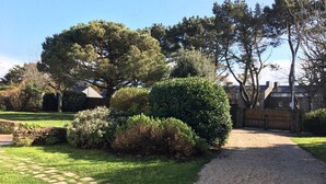 A gravel driveway leading to a gated entrance, surrounded by well-maintained lawns and dense shrubbery. - Maison Proche Plage Pour 8 Avec Jardin et Internet (ARZON)