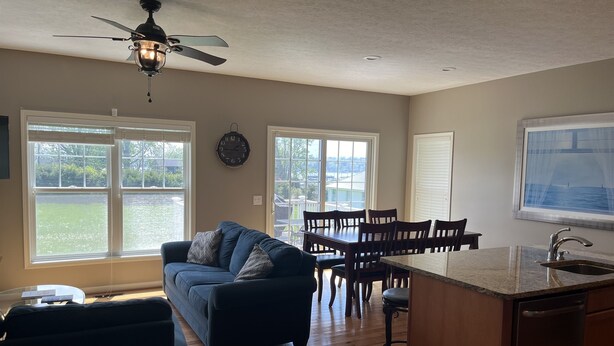 A spacious kitchen with a dining area, wooden flooring, and large windows offering a view of the outdoors. - Bayview at Three Schooners Landing (Sodus Point)