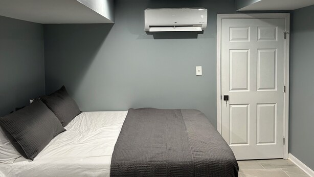 A bedroom with a bed, pillows, an air conditioner, and a door. - Sheridan Lodge is a vibrant and safe neighborhood in Washington, DC. (Washington)