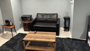 A living room with a black leather sofa, a wooden coffee table, a black side table with a lamp, and a small side table with a coffee maker. - Sheridan Lodge is a vibrant and safe neighborhood in Washington, DC. (Washington)