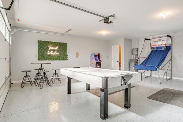 Een kamer met een pooltafel, krukken, een neonbord, een groene muur en een trampoline.