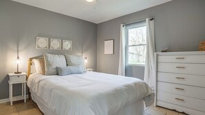 A bedroom with a bed, nightstands, a dresser, and wall art. - Benton Harbor Home w/ Fire Pit - 2 Mi to Beach! (Benton Harbor)