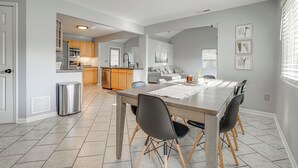 A modern kitchen with a dining area, featuring a large wooden table, black chairs, and a tiled floor. - Benton Harbor Home w/ Fire Pit - 2 Mi to Beach! (Benton Harbor)