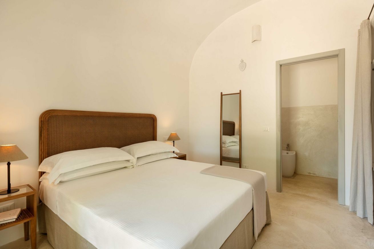A neatly made bed with white linens, a wooden headboard, and two bedside lamps.