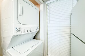A compact, white front-loading washer and dryer unit with control knobs and a small shelf. - The Whaler 3A | Beachfront | Walking Distance to The Hangout | My Beach Getaways (Gulf Shores)