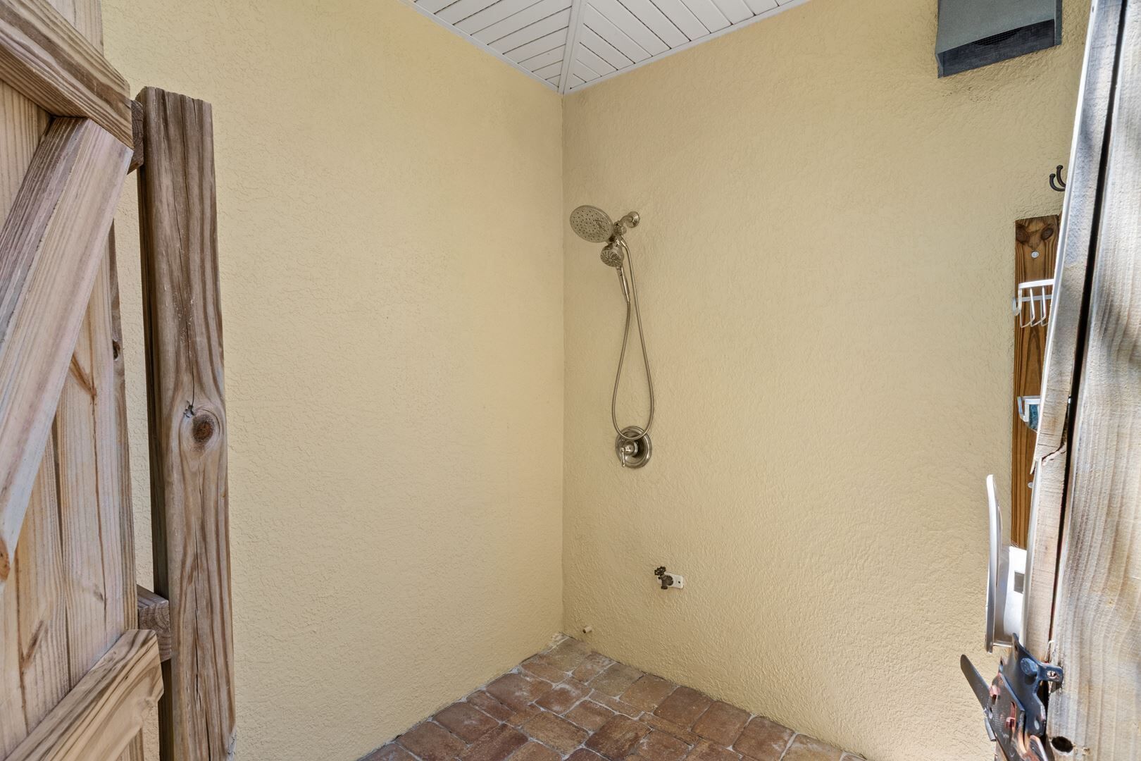 A small, enclosed shower area with a wooden door and a showerhead mounted on the wall.