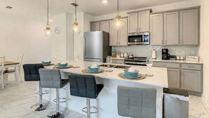A modern kitchen with a central island, bar stools, stainless steel appliances, and pendant lighting. - Modern 4BR Home with Private Pool near Disney (Kissimmee)
