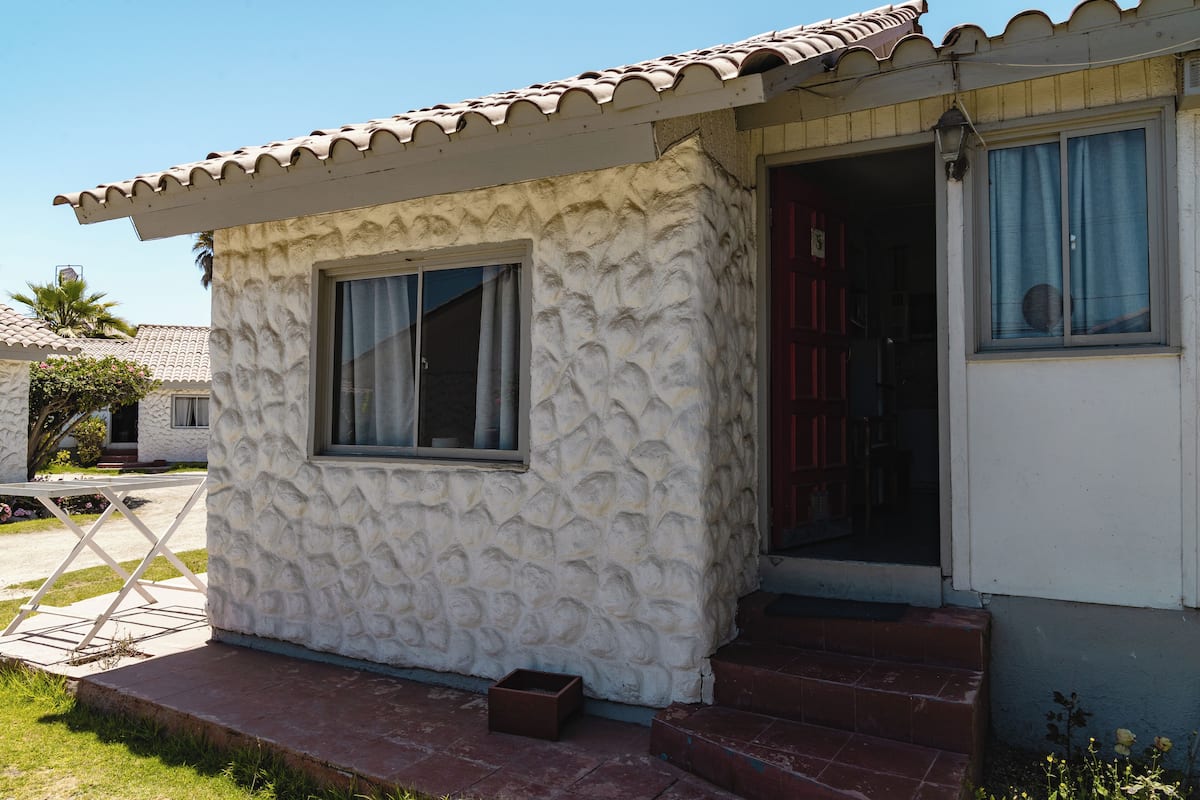 Un edificio pequeño de una sola planta, con fachada texturizada, techo de tejas y puerta principal.