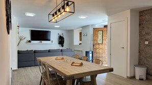 Ein modernes Wohnzimmer mit Esstisch aus Holz, grauem Sofa und Wand-Fernseher.