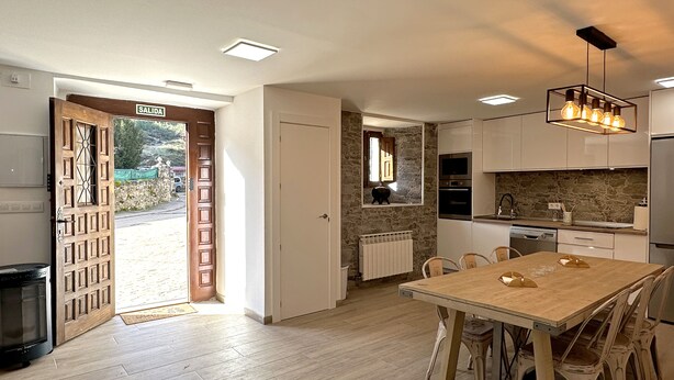 Eine moderne Küche mit Esstisch aus Holz, weißen Schränken und einer Arbeitswand aus Stein.