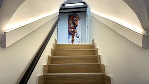 Eine Treppe mit Holzboden und einer Glastür am oberen Ende, die zu einem Raum mit weißen Wänden und einem farbenfrohen Gemälde führt.