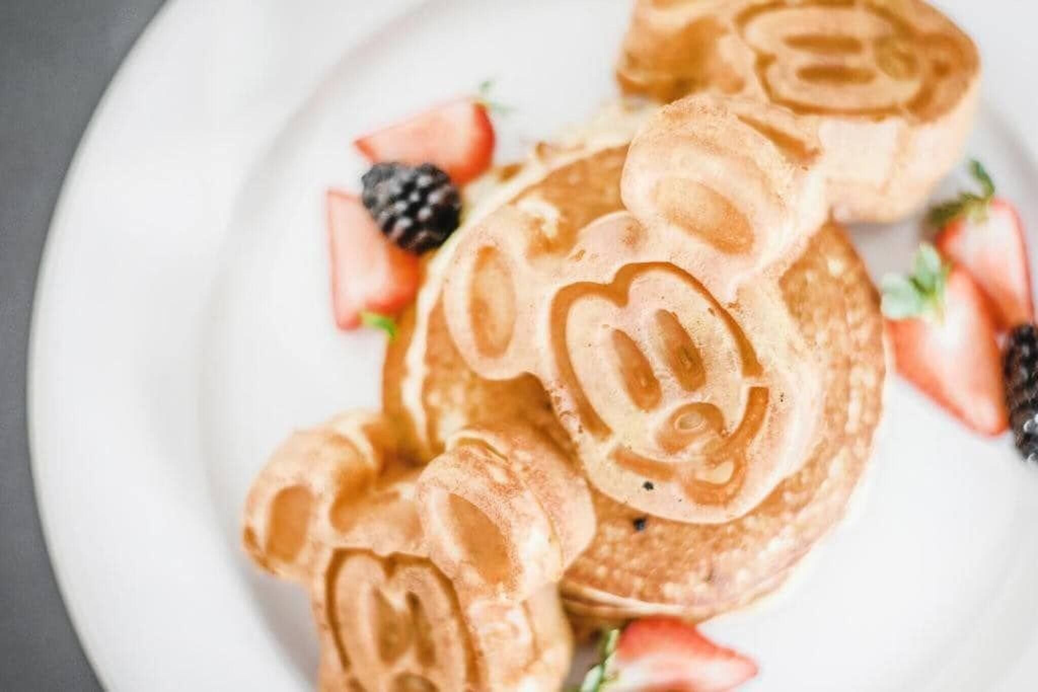 Une pile de crêpes décorées d’un motif en forme de cœur, servies sur une assiette, accompagnées de fraises et de mûres.