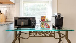 Una cucina con un tavolo in vetro, un forno a microonde, una macchina del caffè e un cesto di snack.