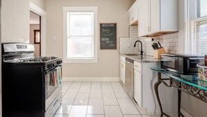 Una cucina con un piano cottura nero, mobili bianchi, un tavolo in vetro e una lavagna con un messaggio di benvenuto.