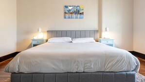 Un letto rifatto con precisione, con una testiera grigia, due comodini con lampade e un quadro appeso al muro.