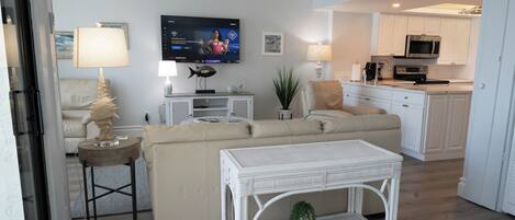 A modern living room with a beige sofa, a white coffee table, and a television mounted on the wall.