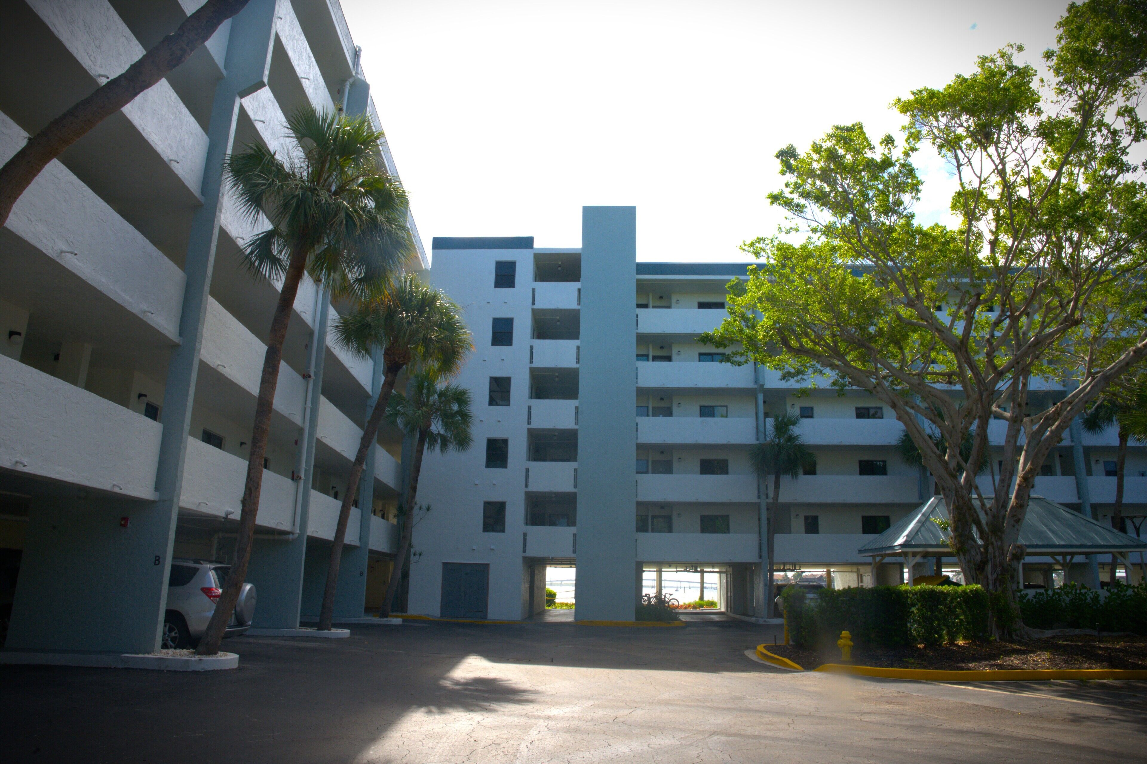 A multi-story parking garage with a central elevator shaft, surrounded by palm trees and a covered area with a roof.