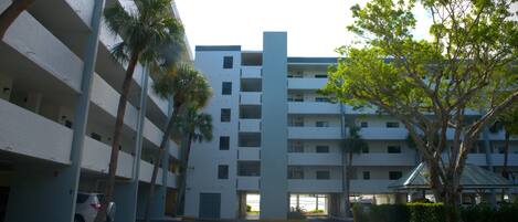 A multi-story parking garage with a central elevator shaft, surrounded by palm trees and a covered area with a roof.