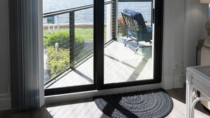 Une pièce dotée d’une porte-fenêtre coulissante donnant sur un balcon avec vue sur une étendue d’eau et un pont.