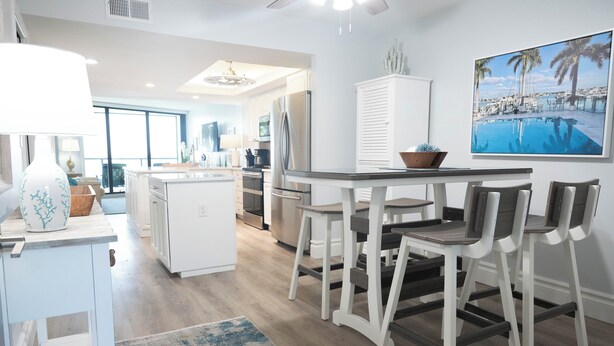 Une cuisine moderne avec des meubles blancs, un coin repas comprenant une table et des chaises, et une grande fenêtre offrant une vue sur l’extérieur.