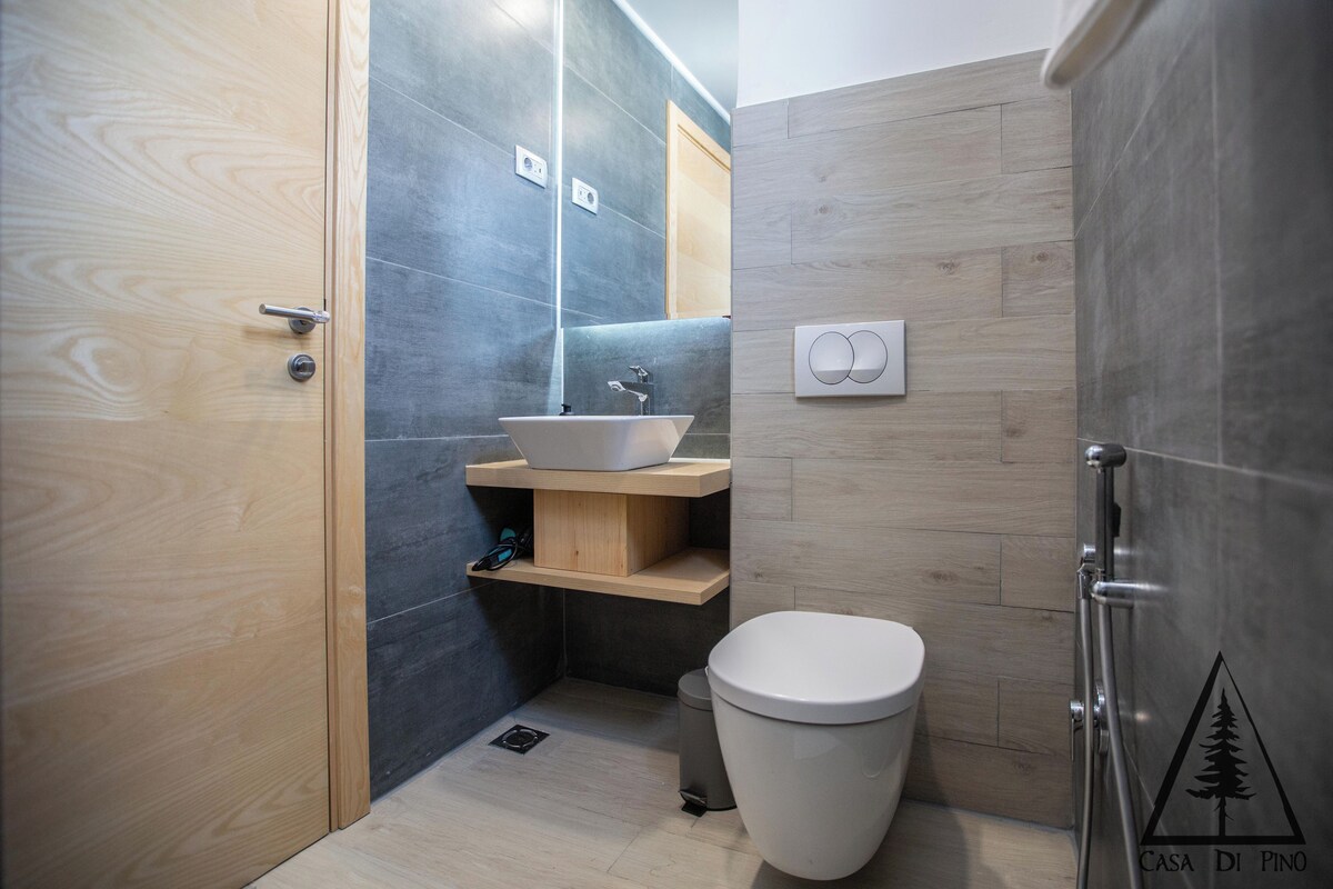 A modern bathroom with a wooden vanity, a white sink, a toilet, and a shower area.