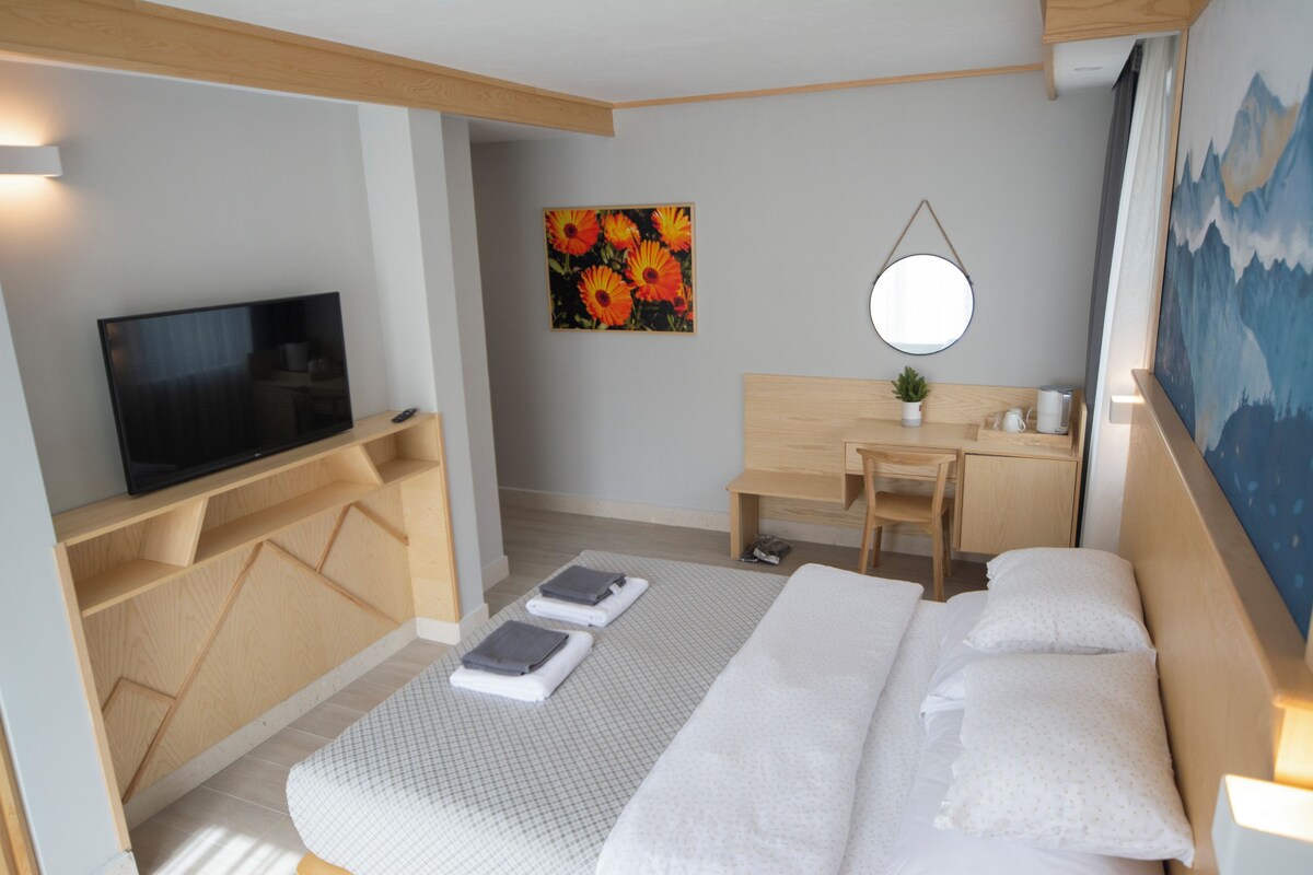 A hotel room with a bed, a desk, a chair, a television, a painting, and a mirror.