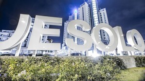 Vista nocturna de un edificio moderno con letras iluminadas de gran tamaño que deletrean "JESOLDO" y un paisaje urbano de fondo.
